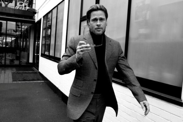 Brad Pitt walking confidently wearing a checkered suit and holding sunglasses