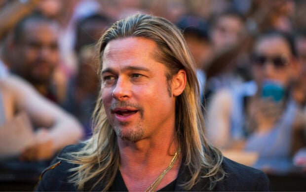 Brad Pitt with long hair and a goatee smiling in a crowd setting