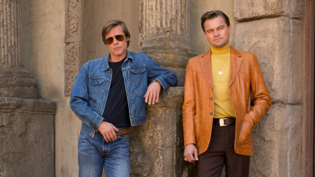 Brad Pitt standing in vintage outfits leaning against a textured stone wall with stylish shades