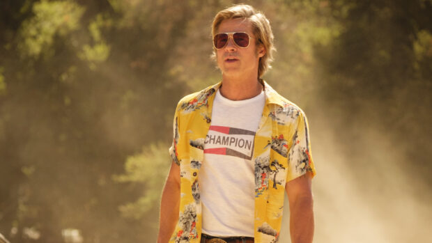 Brad Pitt wearing sunglasses and a yellow shirt walking outdoors in a sunny setting