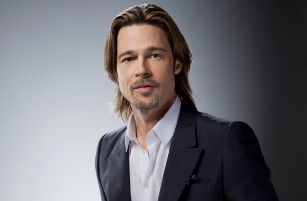 Brad Pitt with long hair and a goatee wearing a dark suit and white shirt