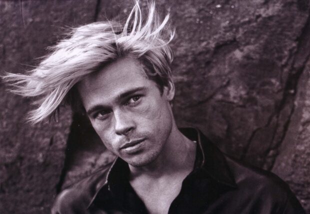 Young Brad Pitt with tousled hair posing against a rocky background