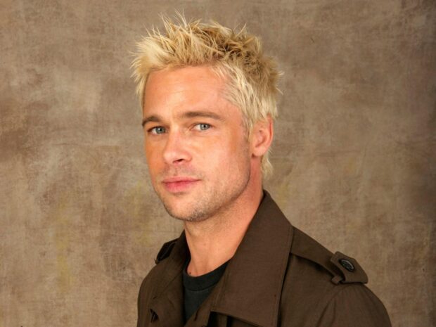 Brad Pitt posing with spiky blonde hair and brown jacket against a textured background
