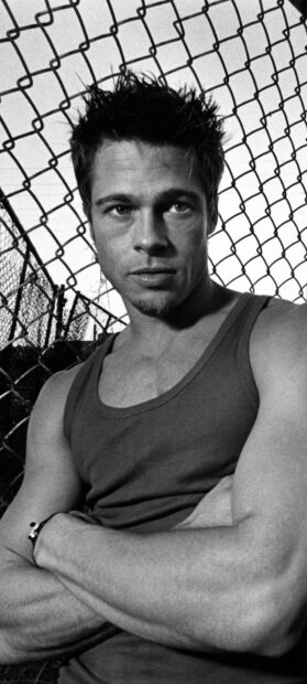 Young Brad Pitt posing with folded arms in front of a chain link fence