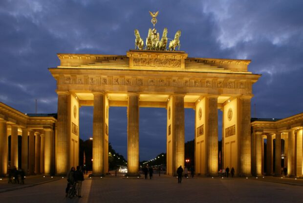 The Brandenburg Gate in Berlin stands illuminated under a cloudy evening sky with people nearby, 2K Desktop Wallpaper