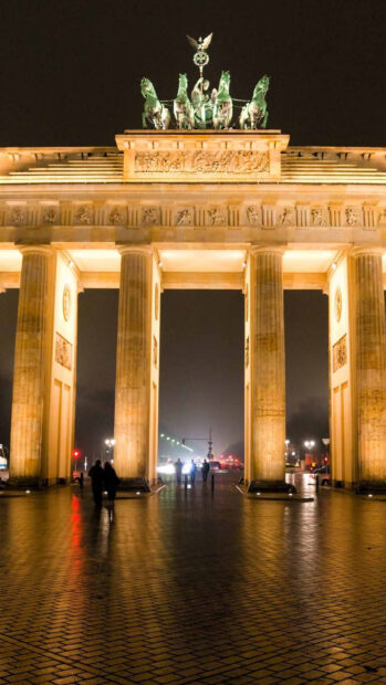 The Brandenburg Gate in Berlin is illuminated with people walking beneath its arches at night, HD Mobile Wallpaper