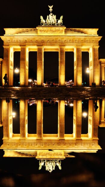 The Brandenburg Gate in Berlin shines brightly reflecting in water during night, 2K Phone Wallpaper