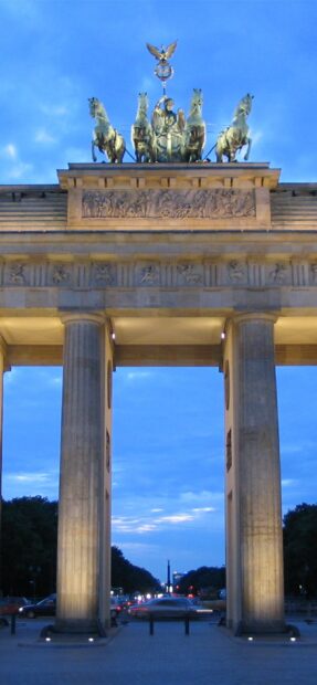 The Brandenburg Gate in Berlin stands illuminated during dusk with cars passing underneath, 2K Mobile Wallpaper