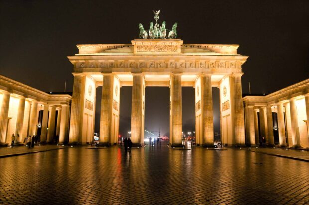 The Brandenburg Gate in Berlin is illuminated warmly with people walking nearby, 2K Desktop Wallpaper