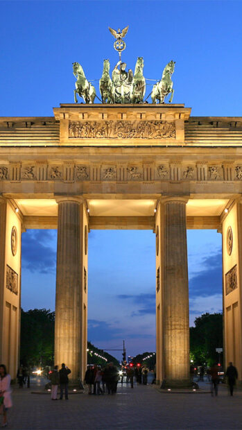 The Brandenburg Gate in Berlin is illuminated with a clear evening sky and people walking nearby, HD Mobile Wallpaper
