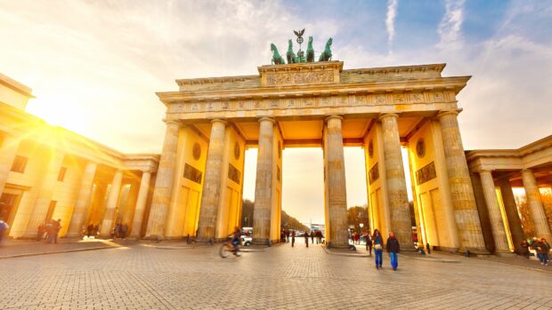 The Brandenburg Gate in Berlin is illuminated by warm sunlight with people walking nearby, 4K Desktop Wallpaper
