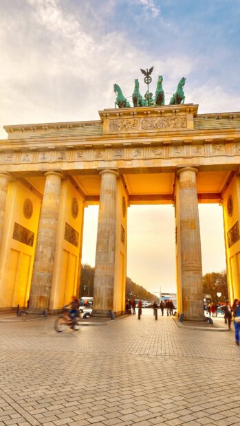 The Brandenburg Gate in Berlin stands tall with people and a cyclist passing through it, 4K Phone Wallpaper