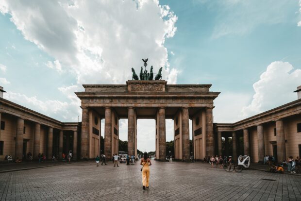 A woman walks toward the Brandenburg Gate in Berlin under a cloudy sky, 2K Desktop Wallpaper