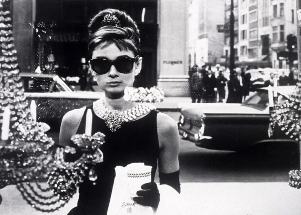 Audrey Hepburn wearing sunglasses and holding a coffee cup in a classic Breakfast At Tiffanys scene