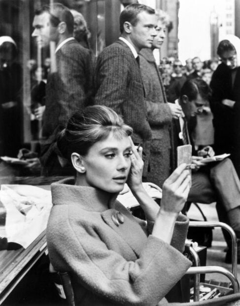 Audrey Hepburn from Breakfast At Tiffanys adjusting her makeup in a public setting
