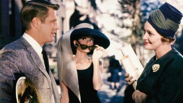 A stylish woman wearing a large hat and sunglasses in a Breakfast At Tiffanys scene