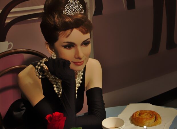 Woman in classic Breakfast At Tiffanys dress wearing pearls and gloves with a rose and pastry on the table
