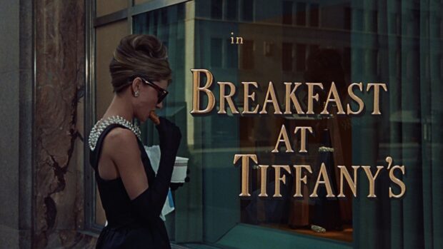 A woman wearing pearls and sunglasses eating breakfast outside a Tiffanys store in Breakfast At Tiffanys