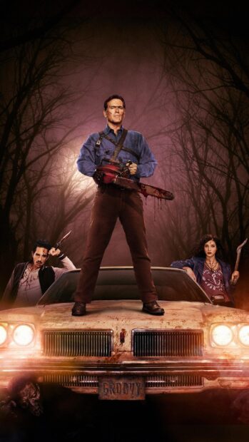 Bruce Campbell stands on a car hood holding a bloody chainsaw with two companions in a dark forest, 2K Mobile Wallpaper