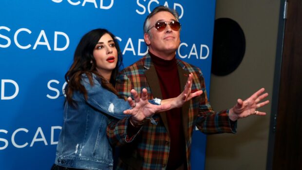 Bruce Campbell wallpapers show him with a woman striking a playful pose in front of a blue SCAD backdrop, 2K Desktop Wallpaper