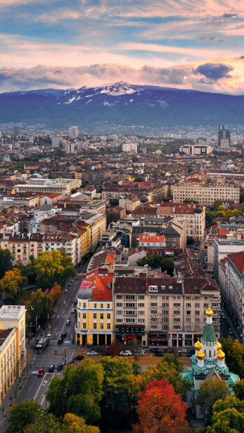 A vibrant view of Bulgaria with city buildings and mountains at sunset, 2K Mobile Wallpaper