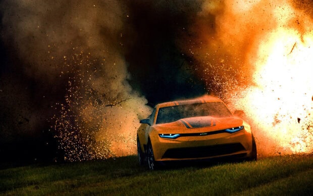 A yellow sports car is driving fast through grass with an explosion of sparks and smoke behind it