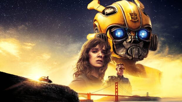 Bumblebee robot with glowing blue eyes stands behind a young woman and a man near the Golden Gate Bridge at sunset