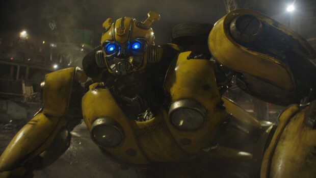 A close up of Bumblebee robot with glowing blue eyes in a dark, smoky environment