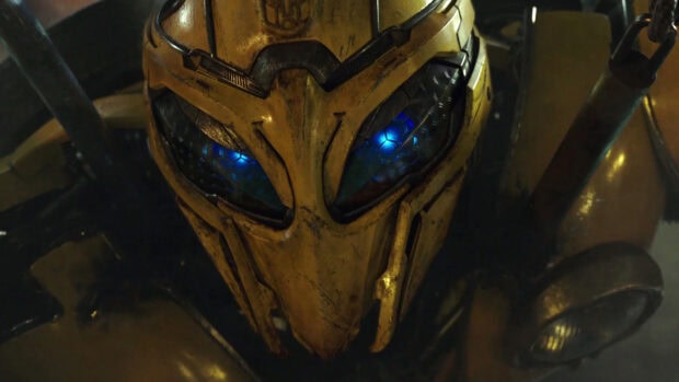 A close up of Bumblebee robot's yellow armored helmet with glowing blue eyes in dark background
