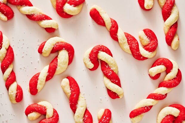 Red and white twisted candy cane cookies sprinkled with sugar on a white surface