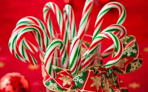 Glass filled with candy cane sticks decorated with a Christmas ribbon on a red background