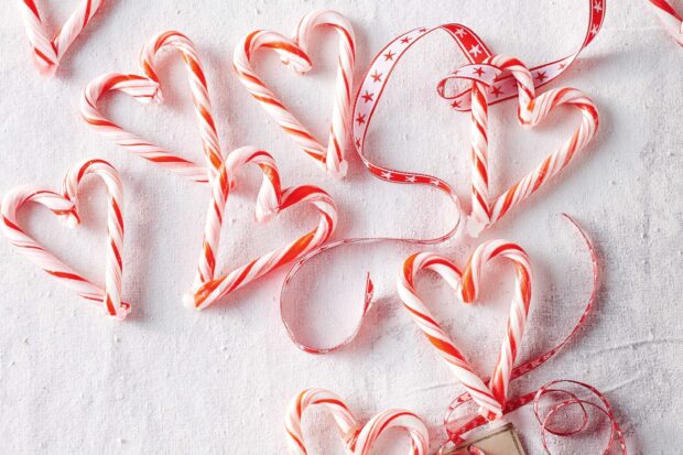 Heart shaped candy cane arranged with ribbons on a white textured surface