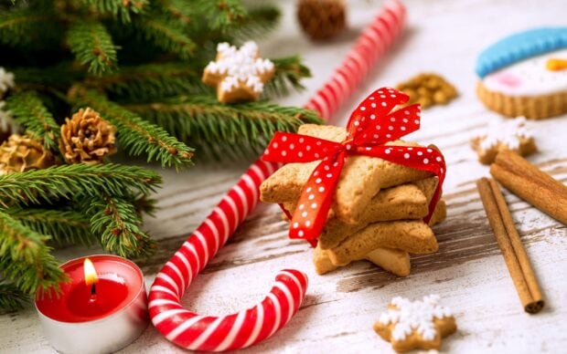 Red and white candy cane next to star shaped cookies tied with a red ribbon on a wooden table