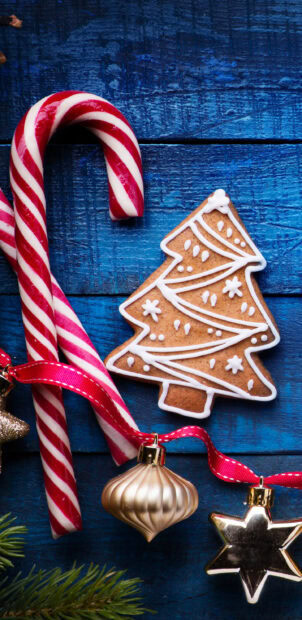 A festive candy cane with a gingerbread tree cookie and Christmas ornaments on a blue wooden surface
