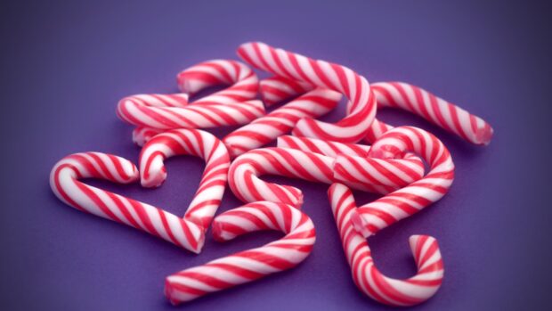 Red and white striped candy cane arranged in a heart shape on a purple surface