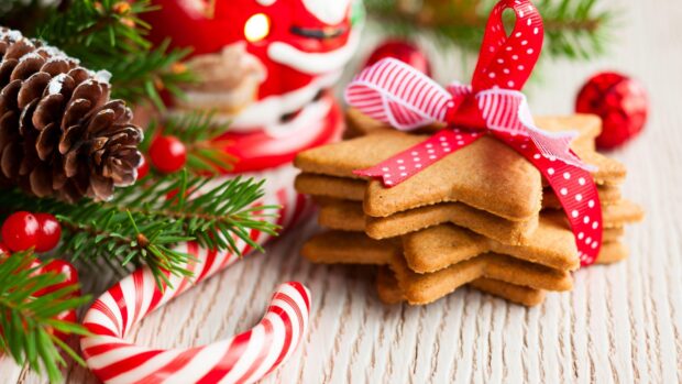 A festive candy cane next to star shaped cookies tied with a ribbon and pine branches