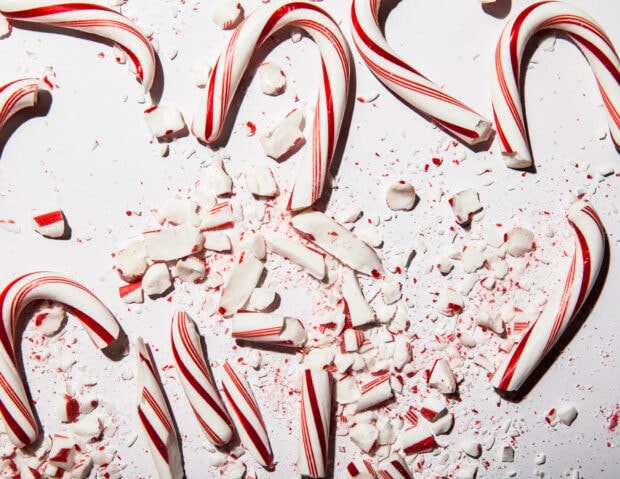 Broken candy cane sticks scattered on a white surface with peppermint pieces and crushed candy cane fragments