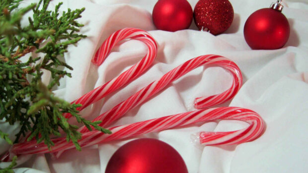 Red and white striped candy cane with Christmas ornaments and green pine branch on white fabric