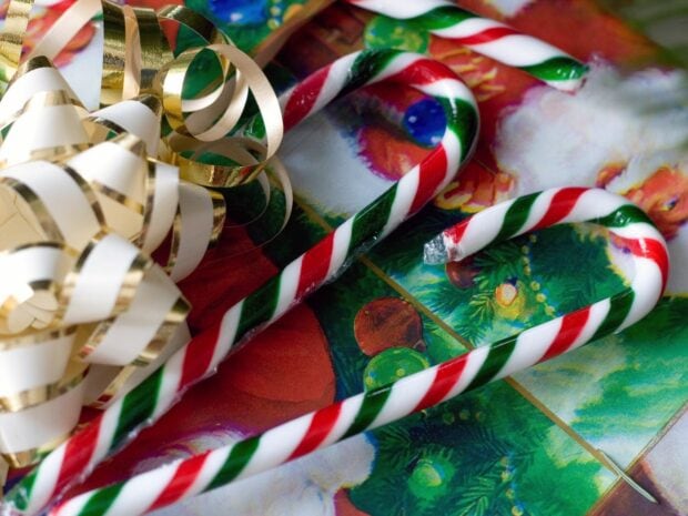 Two colorful candy canes with red and green stripes on a festive Christmas wrapping paper background
