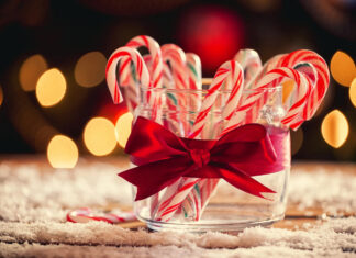 Glass jar filled with candy cane sticks tied with a red ribbon on a snowy surface