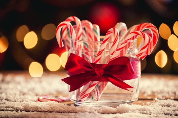 Glass jar filled with candy cane sticks tied with a red ribbon on a snowy surface