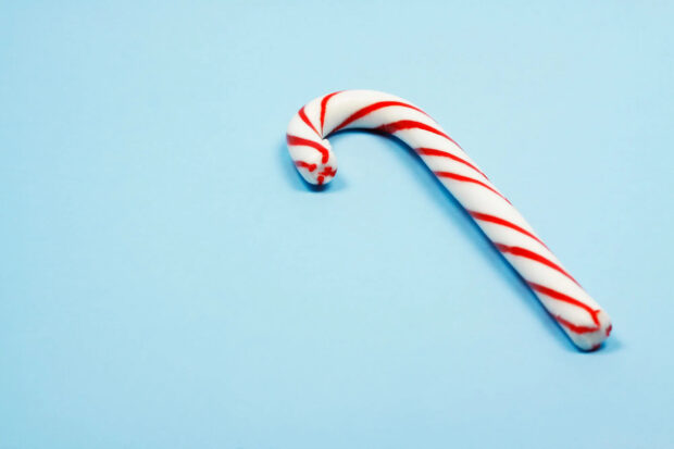A single candy cane with red stripes on a light blue surface