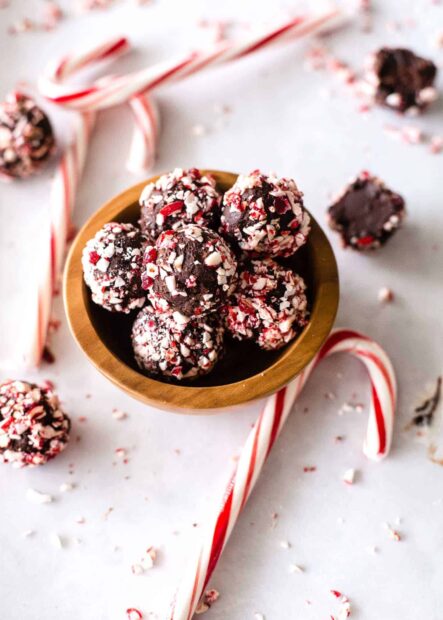 Chocolate truffles coated with crushed candy cane pieces in a wooden bowl surrounded by candy canes