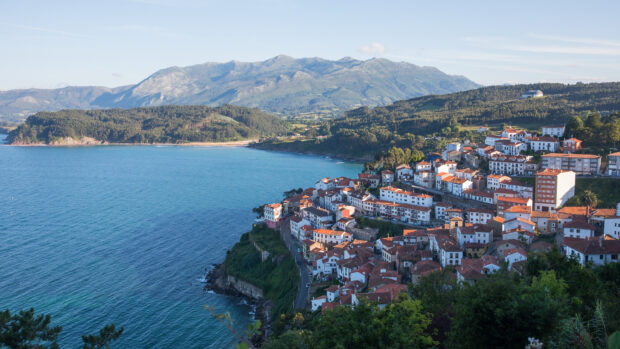 A coastal town with red rooftops overlooking the Cantabrian Mountains and blue sea in clear weather