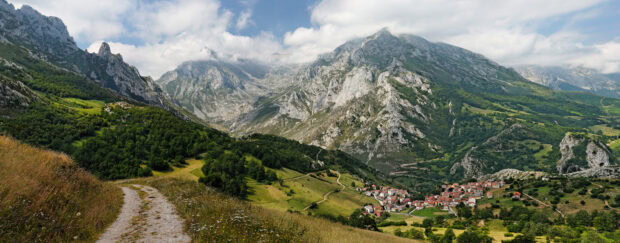 A scenic view of Cantabrian Mountains with a village nestled in the green valley surrounded by rocky peaks and cloudy skies