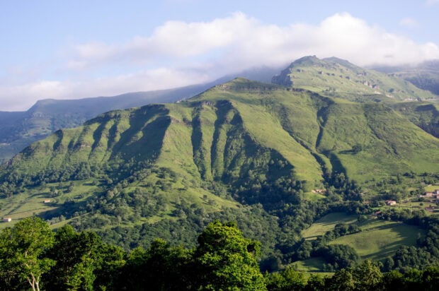 Lush green hills of Cantabrian Mountains covered with trees under a cloudy blue sky