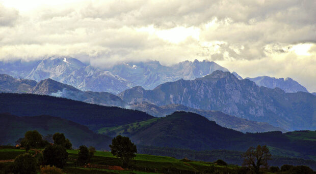 A scenic view of Cantabrian Mountains with cloudy sky and lush green hills in the foreground