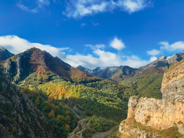 Colorful forests covering the Cantabrian Mountains under a bright blue sky with scattered clouds