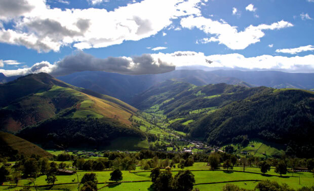 Verdant hills and valleys in the Cantabrian Mountains with scattered trees and cloudy sky