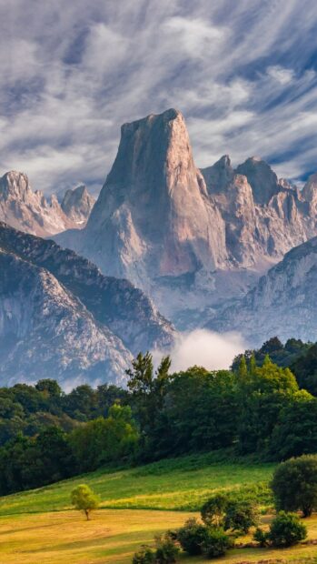 A stunning view of Cantabrian Mountains towering over green forests and fields under a cloudy sky
